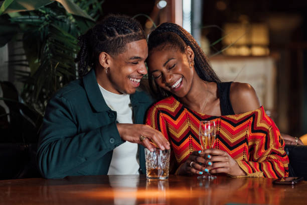 Waist-up shot of young male and female adults having drinks together on a date night. They are both laughing and smiling together leaning into each other.  The restaurant is located in Newcastle Upon Tyne.

Videos are also available for this scenario.